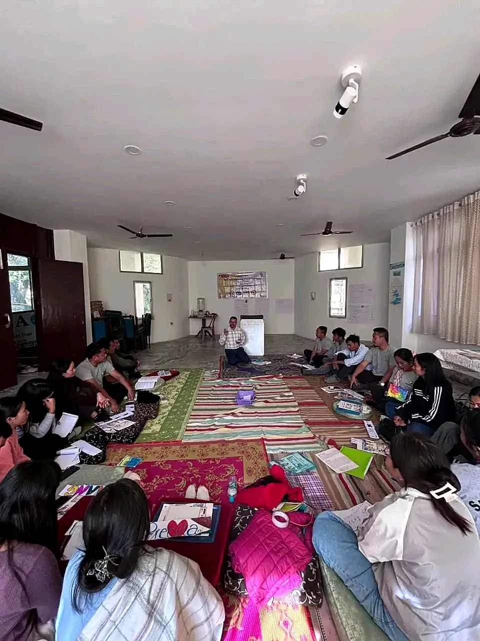 A facilitator leading a session with educators seated in a U-shape on the floor