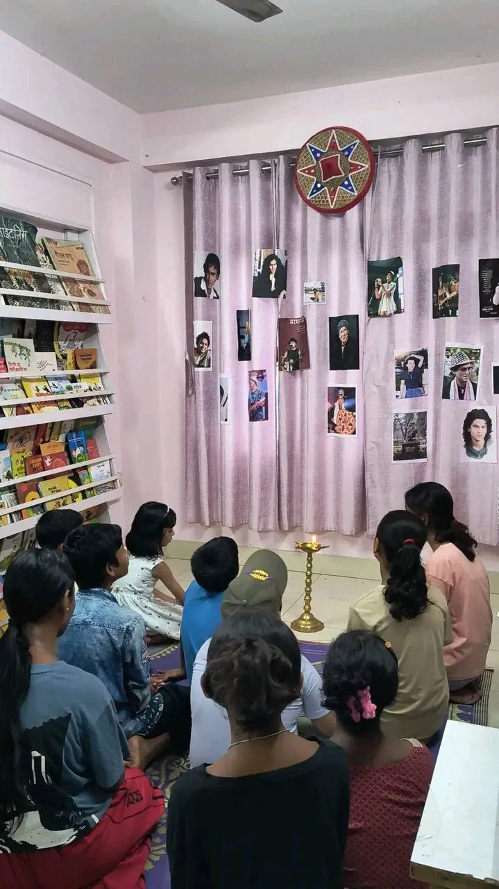 Attendees seated on the floor facing the photo tribute wall and brass lamp during the Zubeen Divas gathering